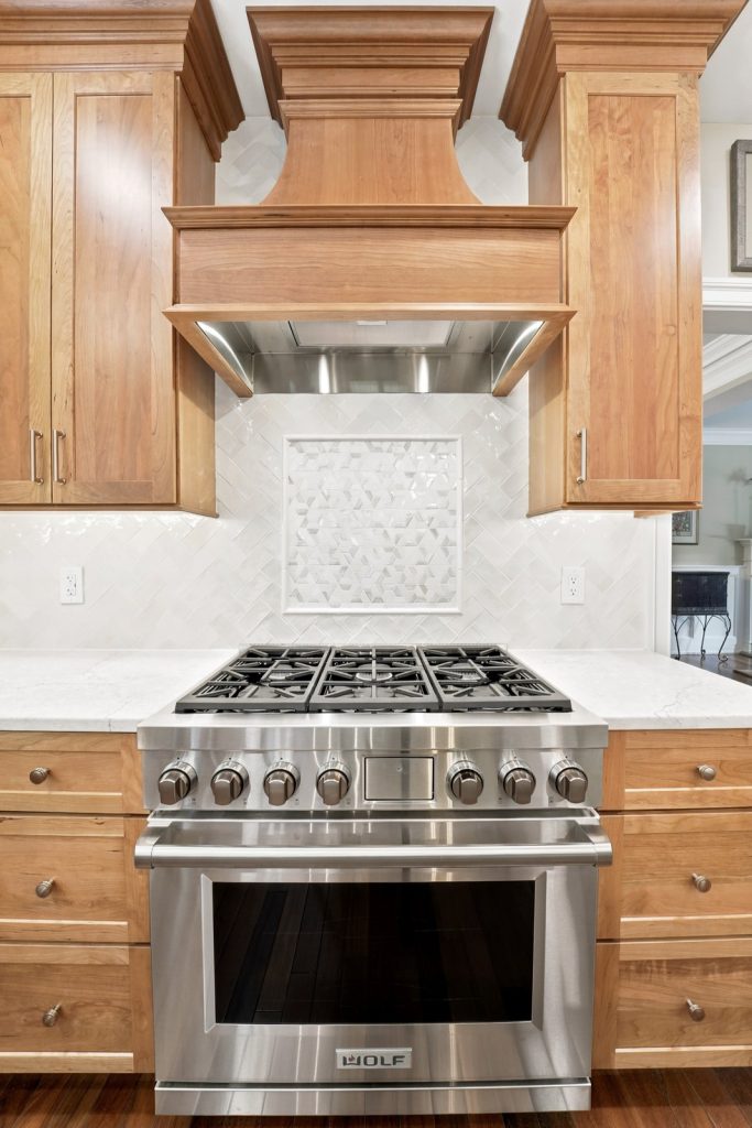 Wolf gas range under a custom carved wood hood in a Phoenixville PA old-world kitchen remodel by Majestic Home Renovations