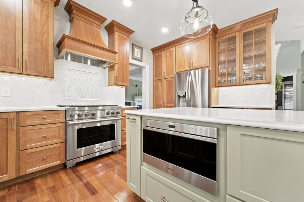 Cherry kitchen cabinetry with a sage island and quartz counters over hardwood floors in Phoenixville PA by Majestic Home Renovations